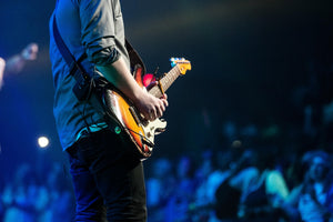 Person playing an electric guitar on stage with a blurred audience in the background